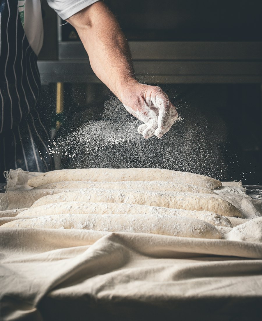 A baker in an apron dusting flour over a wooden work table